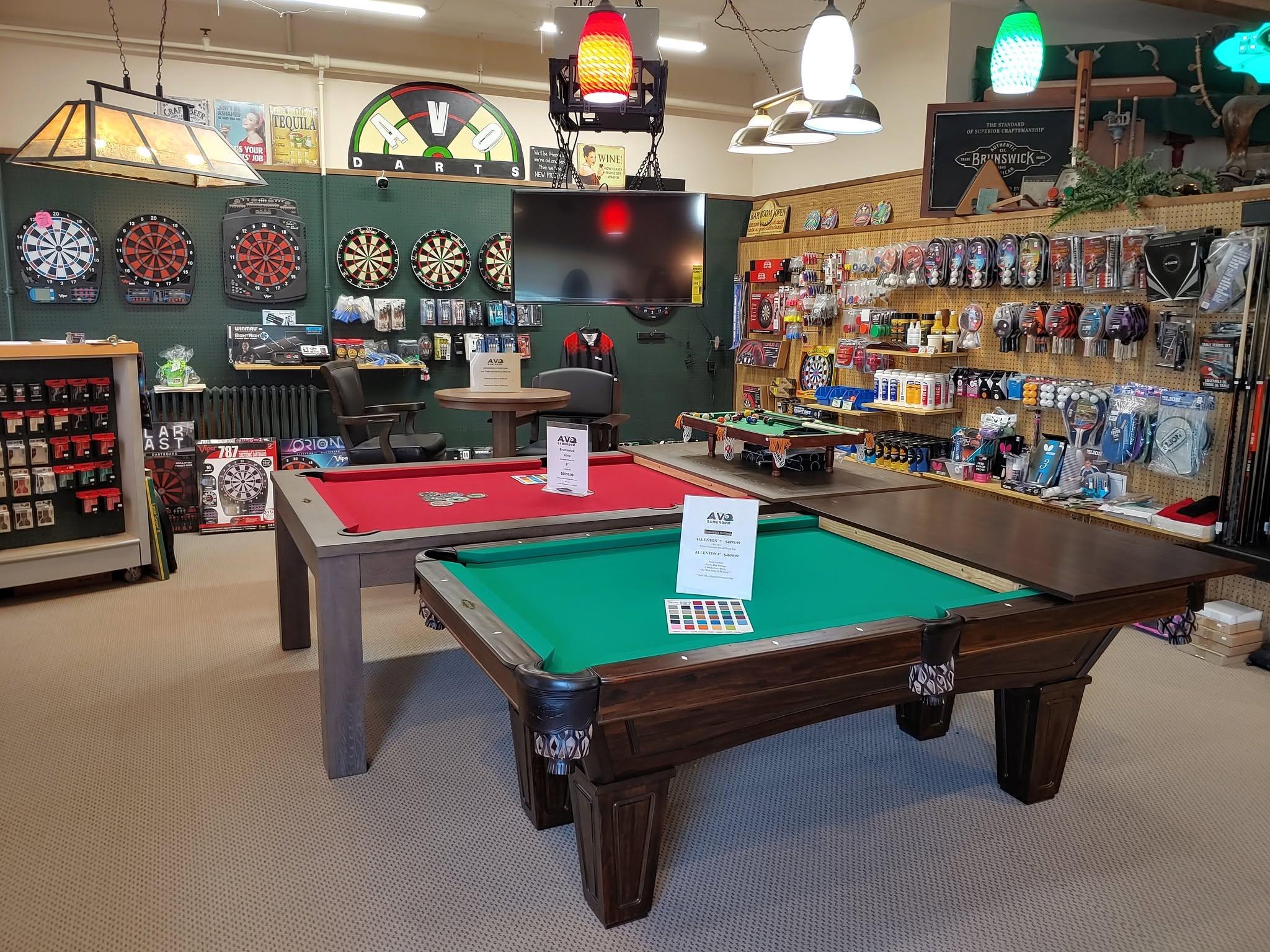 The AVO Gameroom showroom floor: pool tables set up in front of a wall of dart boards, cues, and accessories